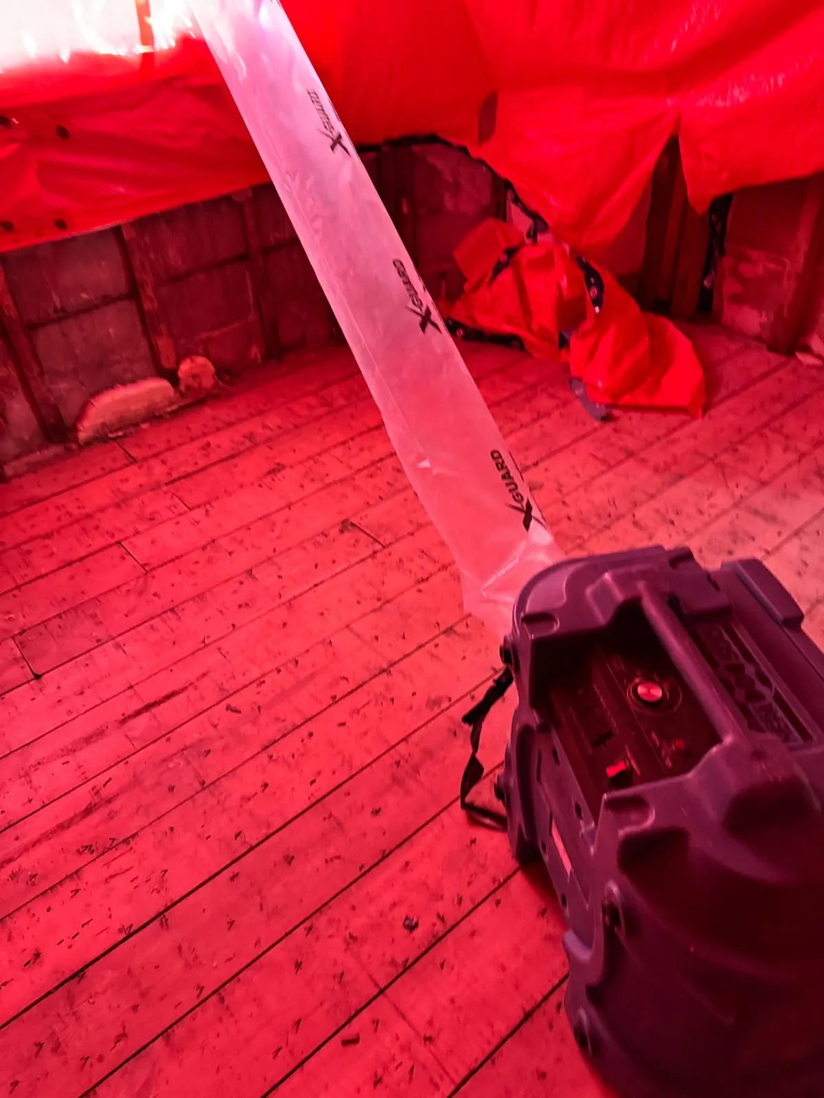 Sealed containment built from red poly sheeting with a clear zippered entry panel, lit by a work light, with equipment staged on the floor inside